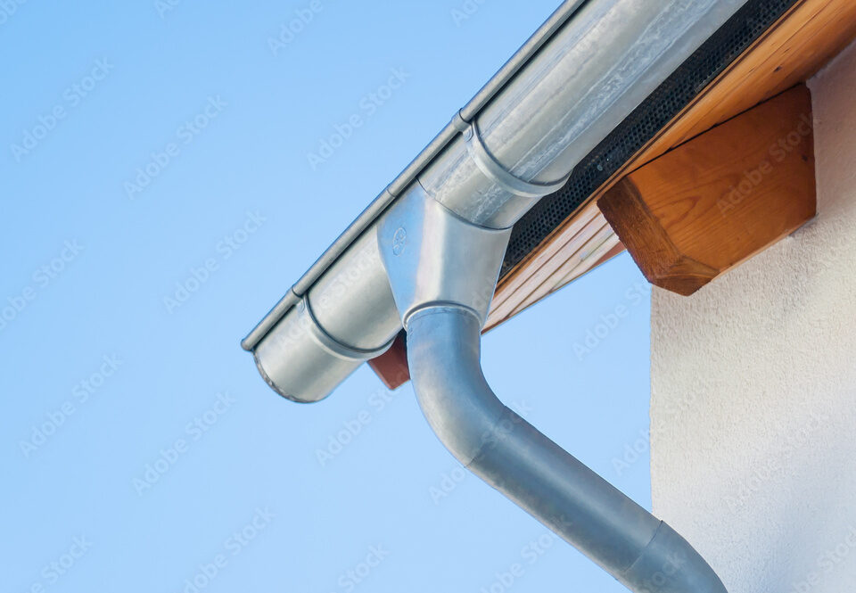 Corner of a house with gutters on a background of blue sky